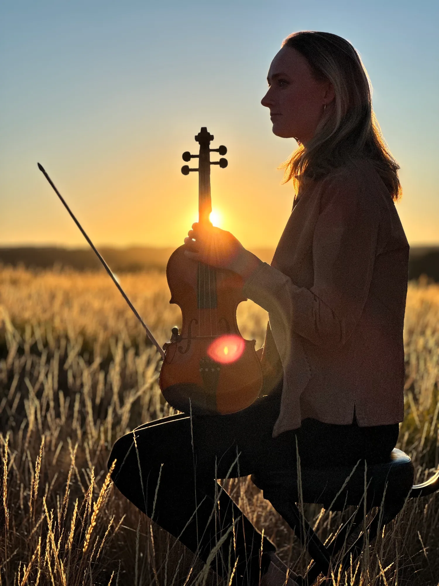 Annie Foxen in profile at golden hour, the sun flaring through her violin
