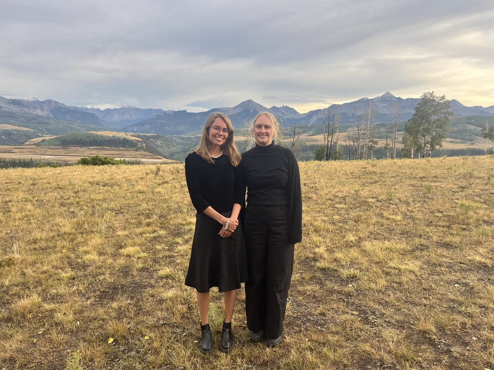 Two performers in a golden field at dusk, the San Juans behind them