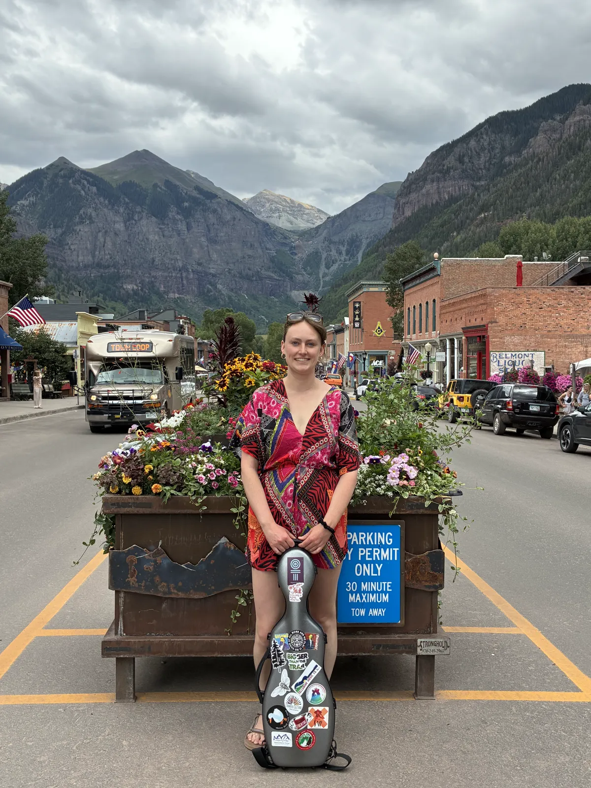 Annie with her violin case on Telluride main street, mountains behind