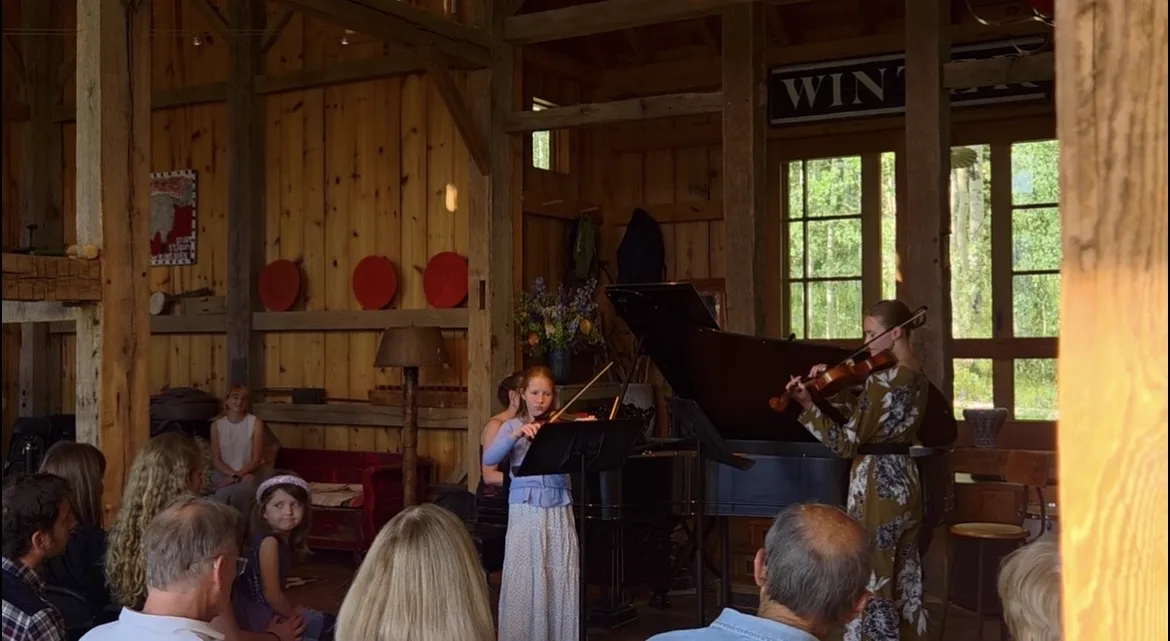 A student performing violin with piano accompaniment at a recital, Annie playing alongside her