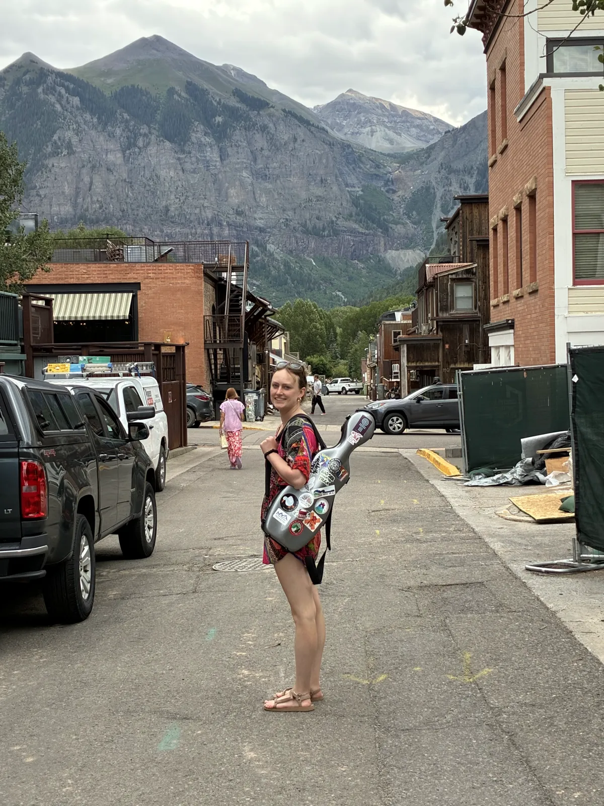 Annie on a Telluride street with her violin case, the San Juans rising behind town